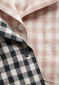 Triibuline särk, millel on ühel poolel roosad ja kreemjad ruudud ning teisel poolel mustad ja kreemjad ruudud, valgete ja mustade nööpidega.