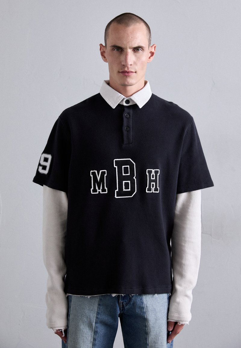 Schwarz, kurzärmeliges Poloshirt mit weißem Kragen, mit "MBH"-Text und der Nummer "19" auf dem Ärmel; strukturiertes Material, gerader Saum.