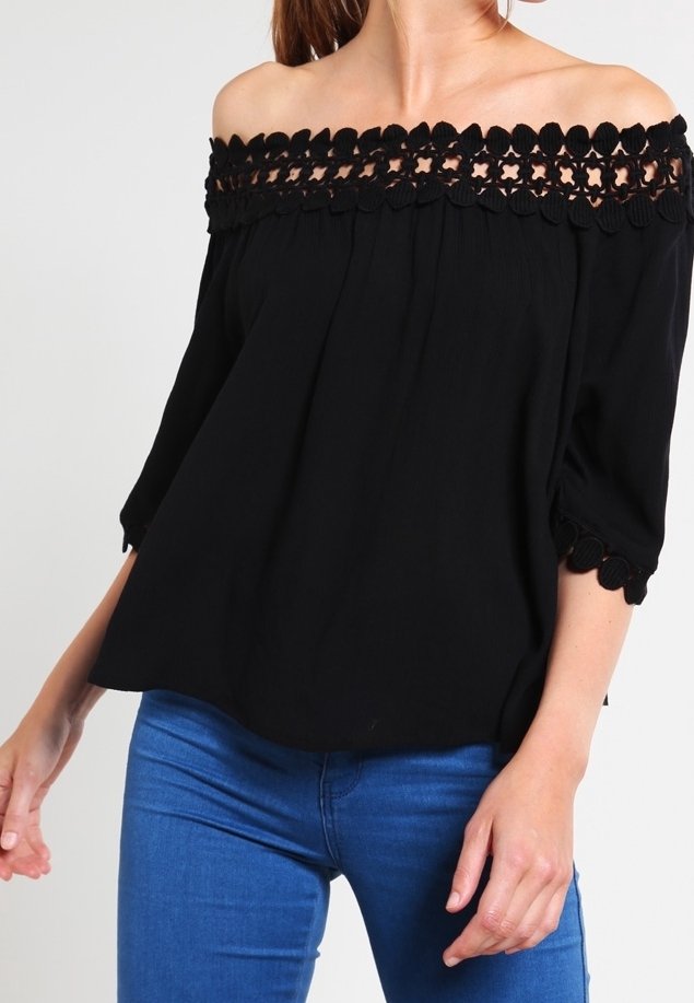 Haut noir décolleté épaules avec bordure en dentelle festonnée, tissu texturé et manches trois-quarts, associé à un jean bleu.