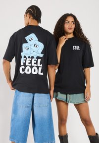 Schwarze Baumwoll-T-Shirts mit Druck auf der Vorder- und Rückseite, die Cartoon-Eiskuben und den Text "FEEL COOL" zeigen. Kombiniert mit hellblauen Jeans-Shorts.