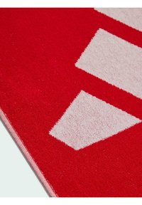 Alfombra roja con grandes formas geométricas blancas, superficie texturizada con una mezcla de fibras y bordes rojos y blancos contrastantes.