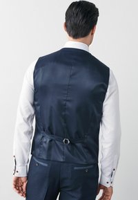 Navy Satin-Weste mit glattem Textur, schlanker Passform und verstellbarem Schnallendetail auf der Rückseite; weißes Hemd mit kontrastierenden Manschetten.