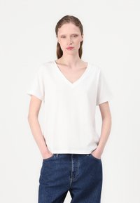 White cotton t-shirt with a V-neckline and short sleeves, featuring a relaxed fit and smooth texture. Paired with dark blue denim jeans.