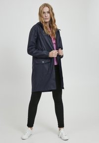 Imperméable marine avec capuche, poignets élastiques et poche avant. Fabriqué en matériau imperméable, il dispose d'une fermeture éclair et d'une coupe décontractée.
