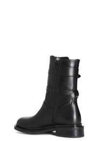 Botín de cuero negro hasta el tobillo con un cierre lateral, que presenta detalles de costura vertical, una puntera redondeada y un tacón plano.