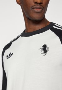 Λευκό και μαύρο βαμβακερό t-shirt με ριμπ λαιμόκοψη, που διαθέτει μαύρο κεντητό λογότυπο δράκου και τρεις ρίγες στα μανίκια.