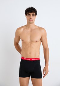 Schwarze Boxer-Shorts mit einem roten elastischen Bund, der das "BJÖRN BORG"-Logo trägt, aus glattem Stoff mit einer engen Passform und einem klassischen Design.