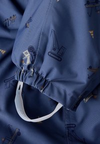 Tejido azul con patrones de temática de construcción, con recogido elástico y un toggle de plástico blanco para ajuste. Textura suave.