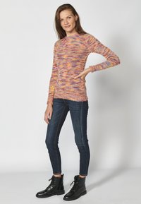 Maglione a maglia multicolore con maniche lunghe, caratterizzato da tonalità pastello e una finitura testurizzata, abbinato a jeans skinny scuri e stivali neri.