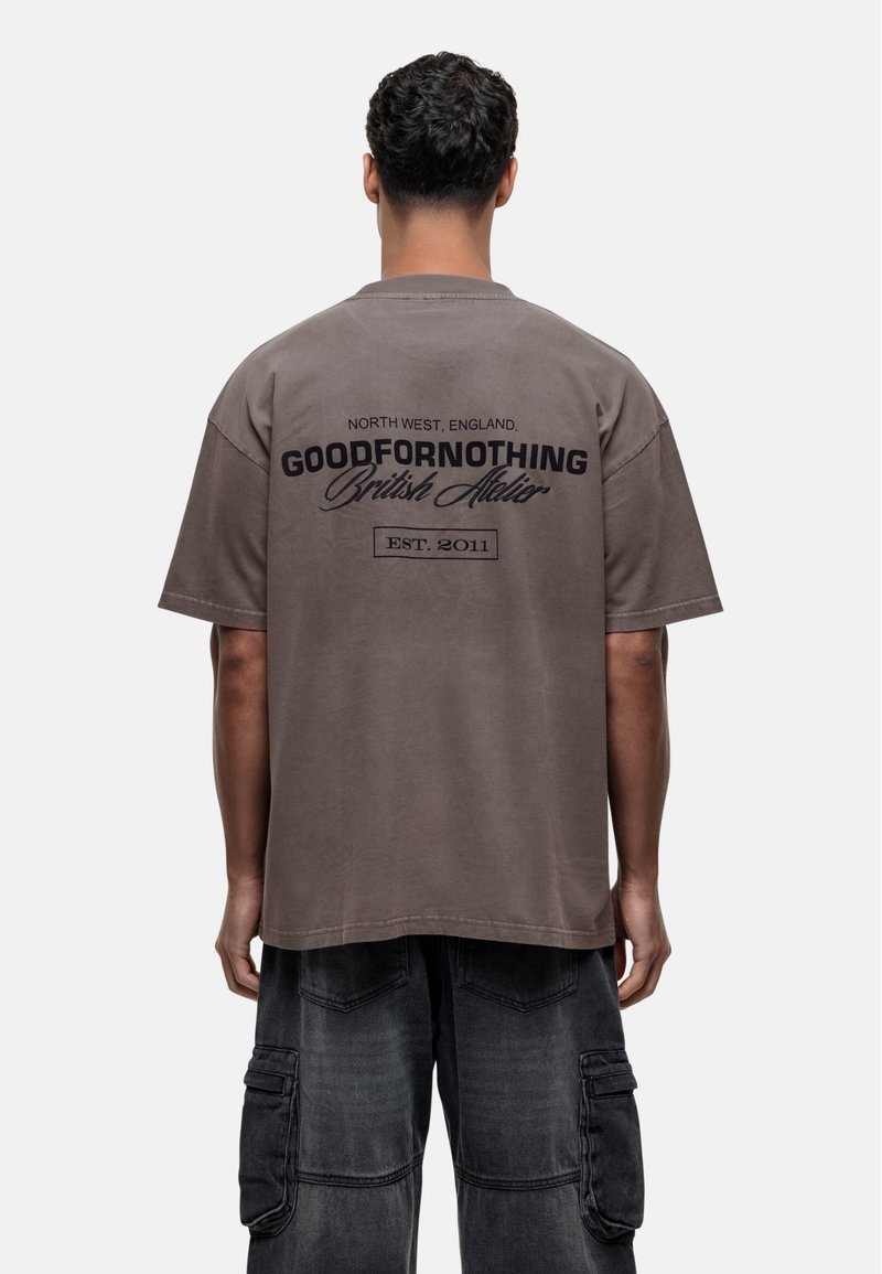 T-shirt en coton marron avec un imprimé graphique au dos, contenant "GOODFORNOTHING British Atelier" et "EST. 2011" en texte sombre.