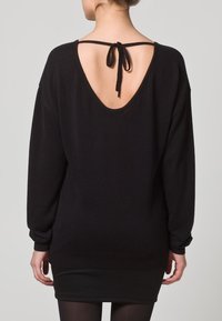 Schwarzer, übergroßer Pullover mit tiefem V-förmigem Rückenausschnitt und Bindeband-Detail. Lange Ärmel und gerippter Saum. Weiche Textur, entworfen für eine lockere Passform.