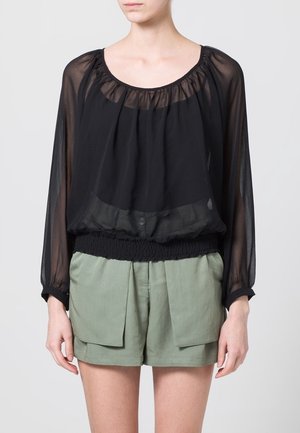 Blouse noire transparente avec un col rond, des épaules froncées et un bas élastiqué, associée à un short tailleur vert olive avec de grandes poches.