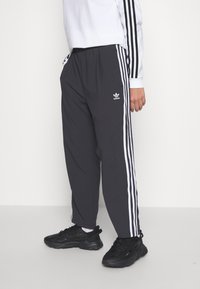 Black athletic pants with three white vertical stripes on each side, elastic waistband, and subtle logo detail near the hip.