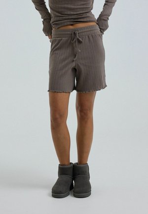 Persona con pantalones cortos de punto gris oscuro con cordón y camiseta de manga larga a juego, combinados con botines grises oscuros, de pie sobre suelo gris.
