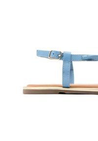 Sandalini azzurri chiari con una sottile cintura e dettaglio fibbia. Suola piatta con una base stratificata beige e marrone. Texture in pelle liscia, design minimalista.