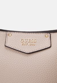 Portefeuille en cuir beige avec surface texturée, présentant un logo doré et des détails de couture. Accentué avec des bordures foncées et des accessoires décoratifs.