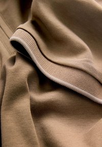 Gros plan sur un tissu beige plié montrant un ourlet côtelé détaillé et une texture tricotée lisse.