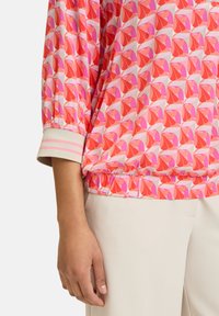 Blusa a maniche lunghe con motivo rosa e rosso, con polsini elasticizzati e orlo arricciato, caratterizzata da un design geometrico e una morbida texture del tessuto.