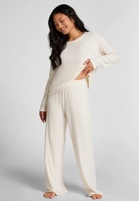 Roomkleurige geribbelde loungewear set bestaande uit een top met lange mouwen en wijde broek, gemaakt van zacht materiaal met een ontspannen pasvorm.