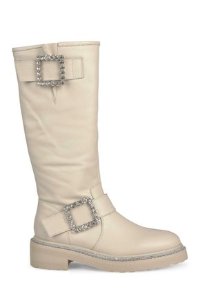 Bottes beige montantes en cuir lisse, dotées de deux grandes boucles carrées ornées de strass et d'une semelle épaisse.