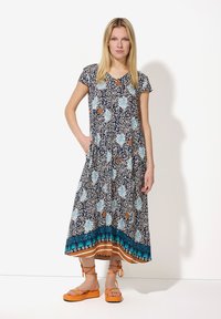 Ein blumengemustertes Kleid mit kurzen Ärmeln, navyfarbener Basis und Knöpfen vorne, mit einem türkis- und braunem Saum. Kombiniert mit orangefarbenen Sandalen.