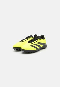 Zapatillas de fútbol amarillas neón con detalles en negro, que cuentan con un material sintético texturizado, diseño de cordones y suela de goma con tacos moldeados.