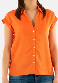 Camisa de manga corta con botones en un brillante color naranja, hecha de una tela suave, con un escote en V y seis botones blancos en la parte delantera.