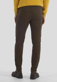 Hnědé texturované kalhoty ve slim fit střihu, s zadními kapsami a okem na pásek, v kombinaci s tmavými kotníkovými botami. Materiál směs bavlny.
