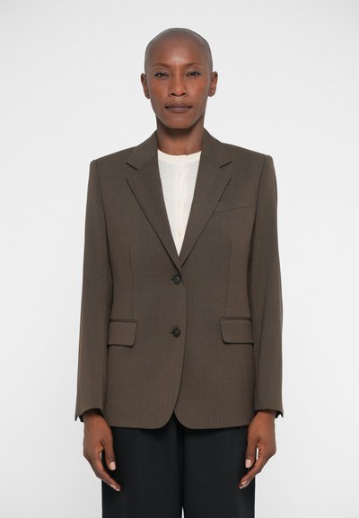 Brown tailored blazer with a notch lapel, two front pockets, and two buttons. Textured fabric and structured fit. Worn over a light top.
