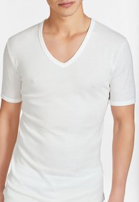 T-shirt bianco a maniche corte con scollatura a V realizzato in tessuto morbido; forma aderente con una texture liscia; presenta un bordo bianco a contrasto sul colletto e sulle maniche.