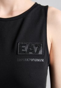 Črna majica brez rokavov z okroglo izrezom, ki se ponaša z teksturiranim vložkom z "EA7" v bisernih podrobnostih in "EMPORIO ARMANI" v srebrni pisanju.