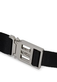 Melna auduma josta ar sudraba metāla sprādzi, kurai ir izteikts logotips, un regulējams siksnas garums drošai aizdarei.