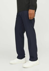 Marinefarbene Hose aus weichem Material, mit geradem Schnitt und leichtem Glanz. Kombiniert mit weißen Turnschuhen, seitliche Ansicht.