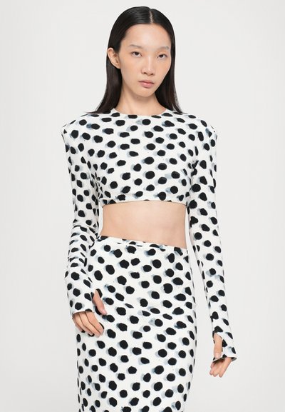 Top scurt cu buline negre și albe, cu mâneci lungi, asortat cu o fustă corespunzătoare, având un material neted și elastic și un design ajustat.