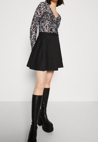 Schwarzer, weit ausgestellter Rock mit einem festen Bund, kombiniert mit einem schwarz-weißen gemusterten Langarmoberteil aus durchscheinendem Stoff. Schwarze Stiefel bis zum Knie.