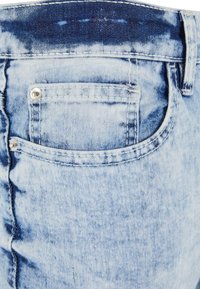 Jeans de mezclilla azul claro con un diseño deslavado, que cuentan con un bolsillo trasero y herrajes plateados en la cintura. Tejido texturizado con costuras visibles.