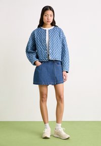 Sinine mustriline tikitud jakk ümmarguse kaelusega ja nuppudega, koos denim-mini seelikuga ja beežide spordijalatsitega.