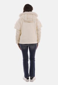 Felpa con cappuccio color crema con materiale trapuntato e imbottito sulle maniche, cappuccio foderato in morbida pelliccia e vestibilità comoda. Abbinata a jeans blu scuro e scarpe da ginnastica bianche.