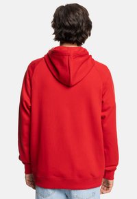 Red hoodie made of soft fabric, featuring a kangaroo pocket, ribbed cuffs, and a hood. Smooth texture with a relaxed fit.