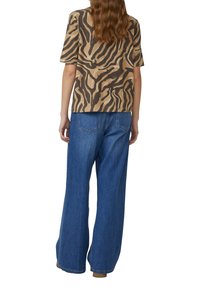 Lühikeste varrukatega pruun ja beežist zebra musteriga särk, millele on sobitatud laiad sinised teksapüksid, millel on plaastrikotid ja mugav lõige.