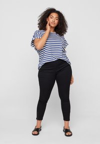 T-shirt à rayures bleu et blanc à manches courtes associé à un jeans skinny noir avec zips latéraux, porté avec des sandales noires.