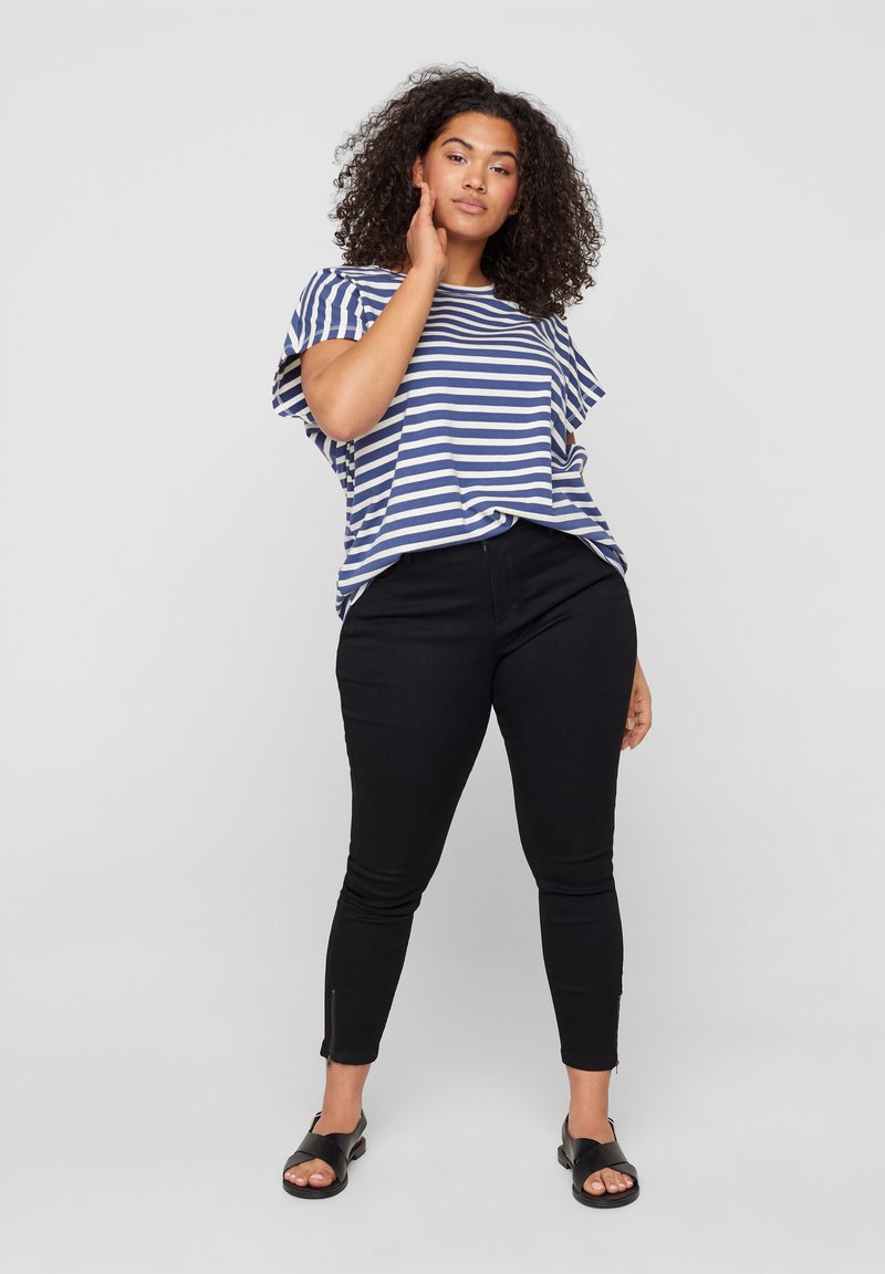 T-shirt à rayures bleu et blanc à manches courtes associé à un jeans skinny noir avec zips latéraux, porté avec des sandales noires.