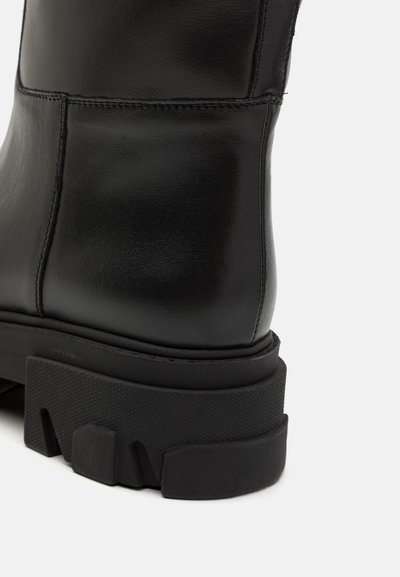 Črne usnjene gležnjarje z gladkim zaključkom, okroglo konico, debelim teksturiranim podplatom in diskretnim šivom ob šivih.