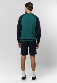 Zaļš un tumši zils džemperis ar raglanu piedurknēm, apvienots ar tumši ziliem šortiem. Iespējas iebūvēti riboti aproces un apakšmala, valkāts ar baltām sporta zeķēm un tumšām kurpēm.