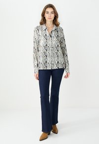 Koszula z długim rękawem zapinana na guziki w wzór węża w odcieniach czerni i beżu, połączona z ciemnymi dzwonami i brązowymi botkami na obcasie.