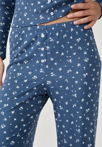 Conjunto de pijama azul con estampado floral que presenta una textura estampada, cierre de botones, mangas largas y pequeños diseños de flores blancas en una tela suave.