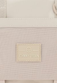 Zaino in tessuto beige con finitura testurizzata, un'accenno crema liscia e una patch rettangolare con il logo che recita "JOHNNY URBAN."