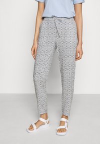 Vzory kalhot v černé a bílé barvě s přiléhavým střihom, páskem na zavazování a zúženými nohavicemi. V kombinaci s bílými sandály na pásečky.