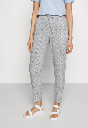 Pantaloni a fantasia in bianco e nero con un design aderente, cintura con lacci e gambe affusolate. Abbinati a sandali bianchi con cinturini.