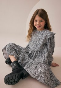 Schwarz-weißes Blumenkleid mit gerüschten Ärmeln, gestuftem Rock, kombiniert mit klobigen schwarzen Stiefeletten mit strukturierten Sohlen.
